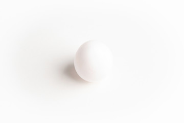 A perfectly standing raw white egg on a plain white paper background.