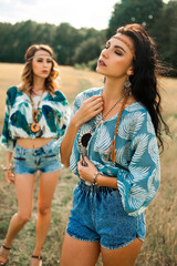 portrait of two beautiful hippie girls, perfect faces, pensive look, trend accessories, pendants, feathers in hair, printed shirts, bohemia, indie, boho style, best friends