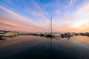 Beautiful port of Alicante, Spain at Mediterranean sea. Luxury yachts, ships, ferries and fishing boats sailing and standing in rows in harbor. Rich people traveling around the world. Sunset evening  