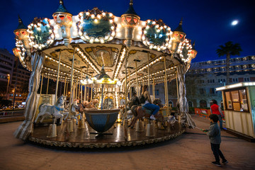Children's vintage Carousel at an amusement park in the evening and night illumination. Beautiful, bright carousel in Alicante, Spain  