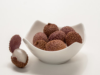 Several lychee fruits, in a white bowl, next to it one with open shell