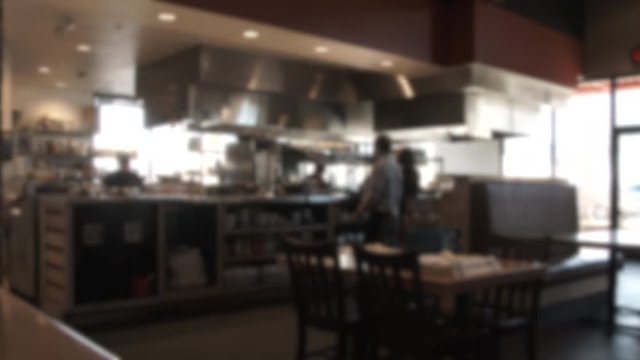 Unrecognizable people in restaurant working in kitchen with servers and wait staff taking orders, soft focus.