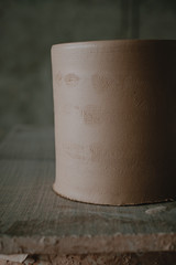 Close-up raw ceramic pottery cup drying on wooden table, clay texture