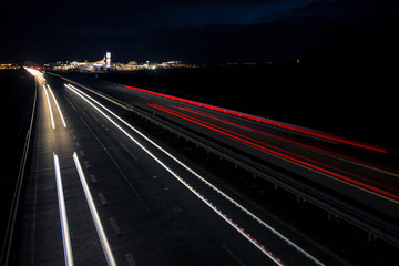 Fototapeta na wymiar Motion blurred light tracks glowing to the darkness of highway traffic to the city just after sunset. Creative long time exposure photography.