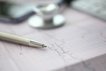 Medical stethoscope head and silver pen lying on