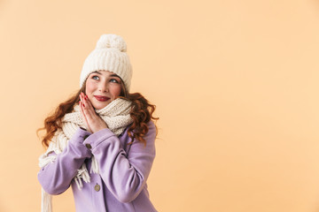 Photo of cute woman 20s in winter clothes smiling, while standing isolated over beige background