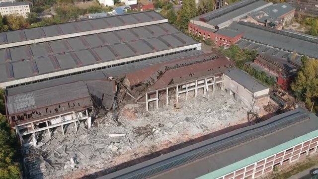 Aerial footage with demolition machinery working on dismantling old industrial buildings, clearing land for new projects