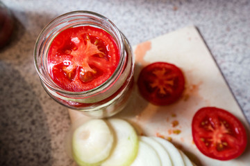 Canning fresh tomatoes with onions in jelly marinade. Woman hands putting red ripe tomato slices and onion rings in jars. Basil, parsley leaves on top of onions. Vegetable salads for winter