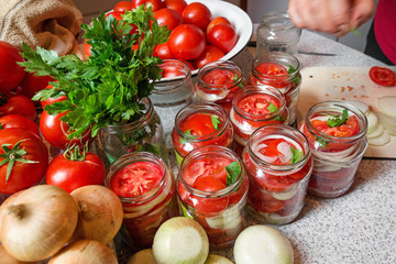 Canning fresh tomatoes with onions in jelly marinade. Woman hands putting red ripe tomato slices and onion rings in jars. Basil, parsley leaves on top of onions. Vegetable salads for winter