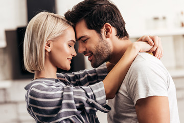 handsome boyfriend and attractive girlfriend hugging and smiling in kitchen