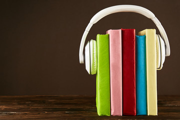 Fototapeta na wymiar Electronic audiobook vs regular paper book concept. Stack of different color hardcover books with blank colorful covers & white headphones on table. Old versus new. Close up, copy space, background.