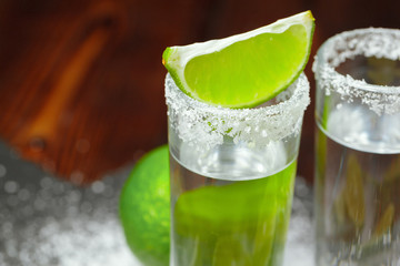 Tequila silver shots with lime slices and salt on wooden board