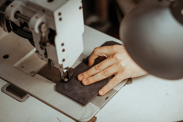 Close up of sewing machine working part with leather. The master's hands sews a leather product. Handmade concept.