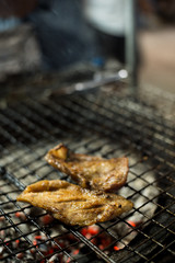 Local roast pork is grilled on a steel grill with hot charcoal below.
