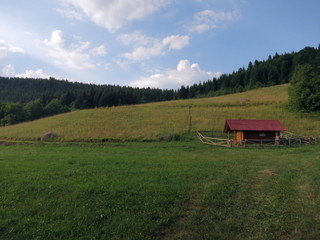 A shepherd's hut on the edge of a field surrounded by forest on a partly cloudy afternoon near Zelenkovac, Republika Srpska, Bosnia and Herzegovina