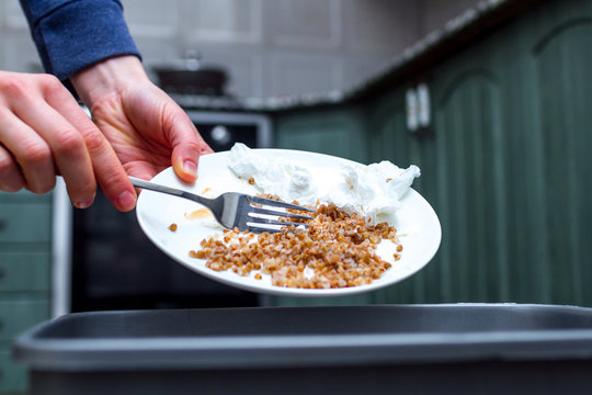 Close up of a person throwing from a plate the leftover of buckwheat to the trash bin. Scraping food waste