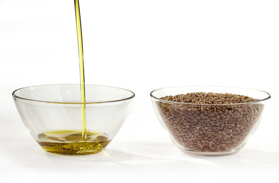 A stream of flowing hempseed oil and hemp seeds in a round glass bowls. Isolated on a white background.
