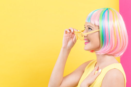 Young woman in a colorful wig with shutter shades sunglasses on a split yellow and pink background
