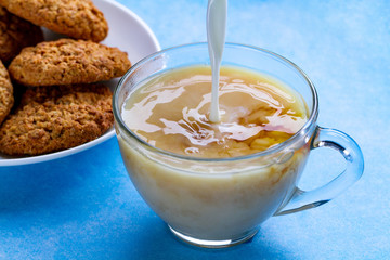 Breakfast with oatmeal cookies and pouring milk into a cup of black tea. Flour, cereal dessert and hot drink