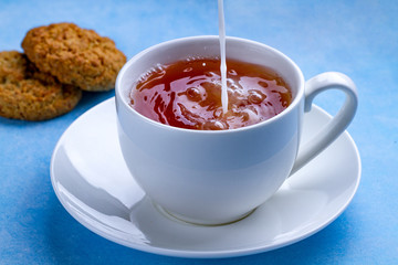 Breakfast with oatmeal cookies and pouring milk into a cup of black tea. Flour, cereal dessert and hot drink