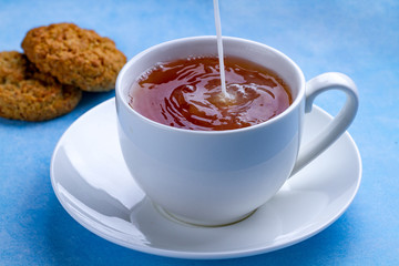 Breakfast with oatmeal cookies and pouring milk into a cup of black tea. Flour, cereal dessert and hot drink