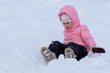 Fototapeta na wymiar a girl in a pink jacket plays in the snow in winter
