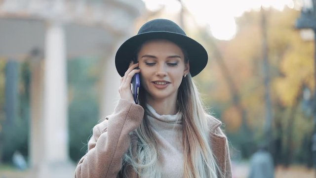 Beautiful attractive woman wearing in coat and hat speaks by phone in the city center on a sunny spring weather