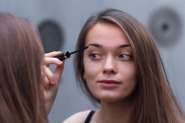 Young, attractive brown hair woman applying black mascara for eyelash makeup in mirror. Home and everyday Makeup