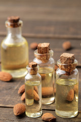 natural almond oil in a glass bottle and fresh almond nuts close-up on a brown wooden table.