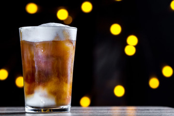 A glass of coffee, cold cocktail with foam and ice on the background of lights