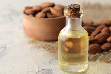 Fototapeta na wymiar natural almond oil in a glass jar and fresh almond nuts on a light concrete background. close-up