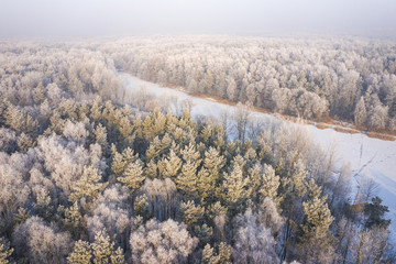 Rime and hoarfrost covering trees. Aerial view of the snow-covered forest and lake from above. Winter scenery. Landscape photo captured with drone.