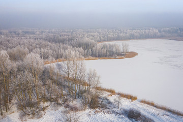 Rime and hoarfrost covering trees. Aerial view of the snow-covered forest and lake from above....