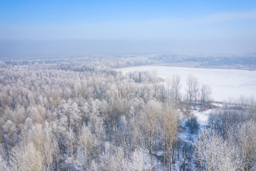 Obraz na płótnie Canvas Rime and hoarfrost covering trees. Aerial view of the snow-covered forest and lake from above. Winter scenery. Landscape photo captured with drone.