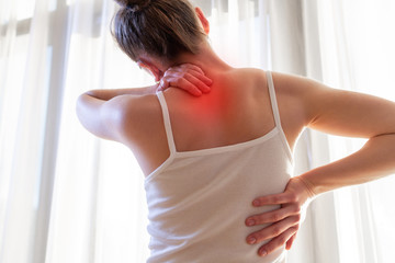 Young woman suffering from neck pain and backache, stretching the muscles.