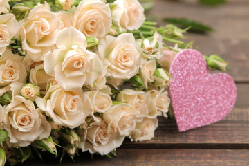 A bouquet of beautiful tender mini roses on a brown wooden table with hearts