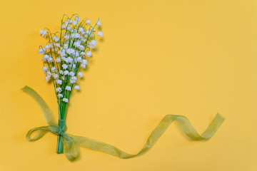 Bouquet of lilies of the valley flowers with green ribbon on bright yellow paper background....