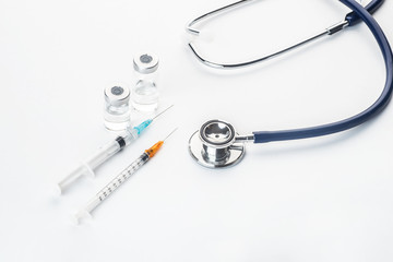 Pills spilling out of pill bottle syringe thermometer and stethoscope on white background
