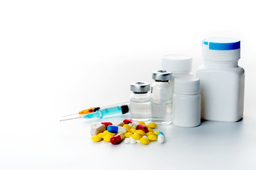 Pills spilling out of pill bottle syringe thermometer and stethoscope on white background