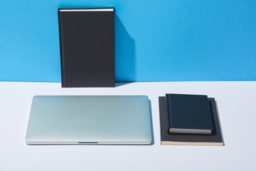 laptop and notebooks on white desk and blue background