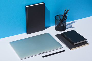 laptop, pencil holder and notebooks on white desk and blue background