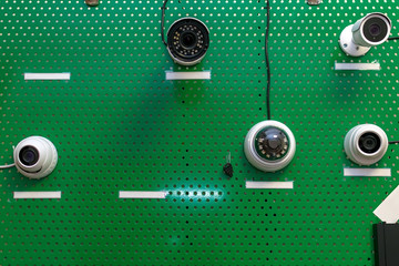 samples of CCTV cameras hung on a green metal stand in the store for demonstration