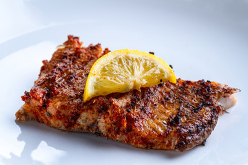 Fresh, grilled salmon fillet with a slice of juicy lemon on a white plate