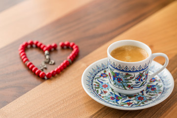 Turkish coffee with heart shaped red rosary on brown table