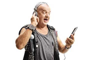 Excited mature man punker in a leather vest holding a mobile phone and listening to music on...