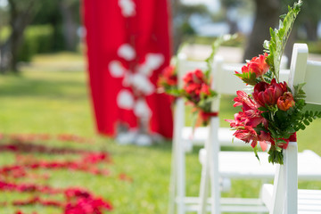 Fototapeta na wymiar chairs decorated with fresh flowers in red tones for the wedding ceremony on the green lawn