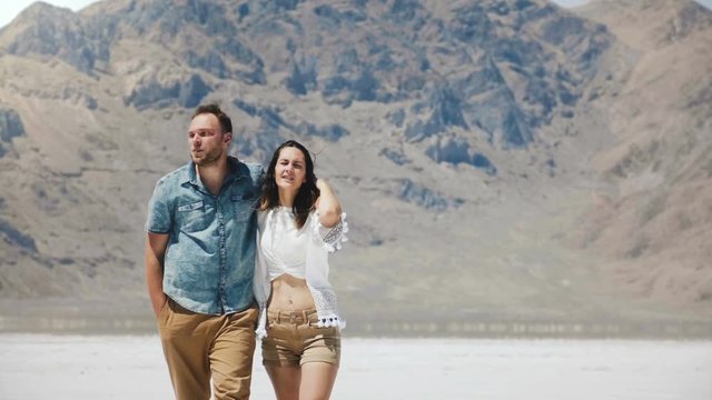 Happy successful Caucasian romantic couple walk hugging and talking cheerfully at salt desert lake in Bonneville Utah.