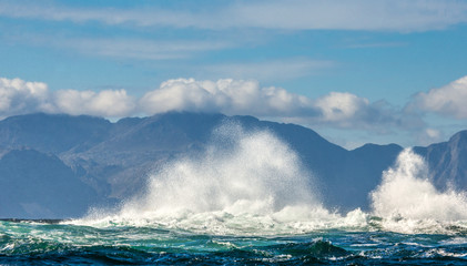 Big waves break on the rocks in the sea against the backdrop of the coastline. Beautiful seascape.  A beautiful moment. Very dynamic photo. Cape Town. False Bay. South Africa.