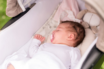 Portrait of a baby girl lying in a stroller in a park on a sunny day.