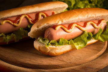 Photo of barbecue grilled hot dog with yellow mustard and ketchup on wooden background. Hot dog sandwich with potato fries and sauces.